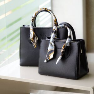 Stylish black leather handbag with decorative handles on a minimalist shelf.