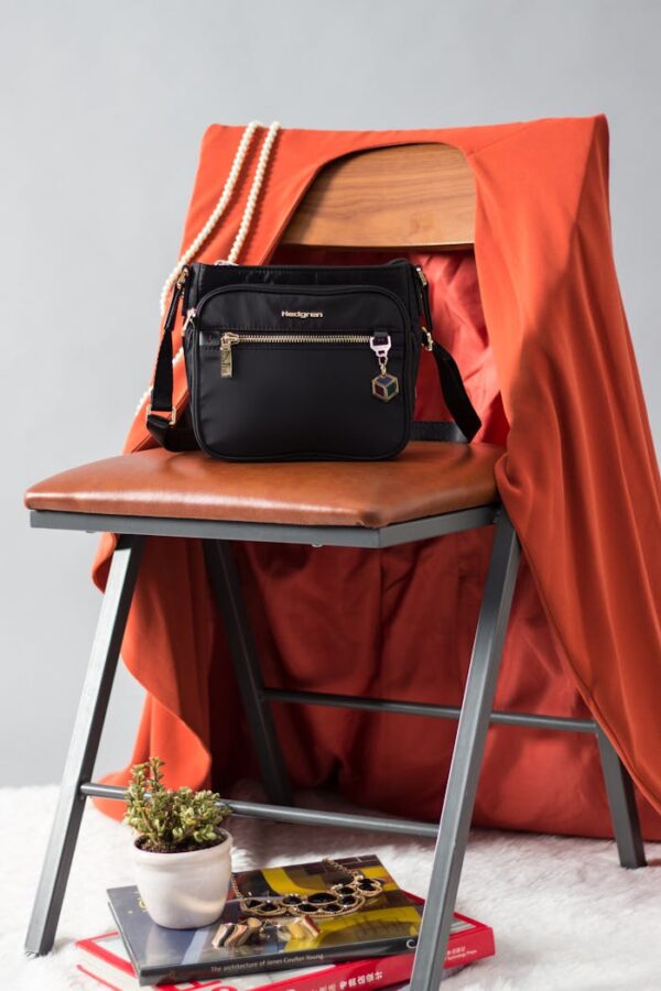 Black handbag on a chair with orange cloth, book, and decorative plant for a modern look.