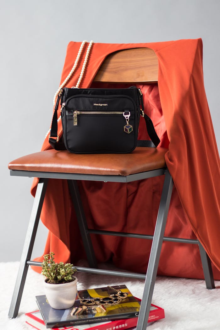 Black handbag on a chair with orange cloth, book, and decorative plant for a modern look.