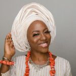 Elegant woman wearing traditional Nigerian headwrap and jewelry, smiling warmly.